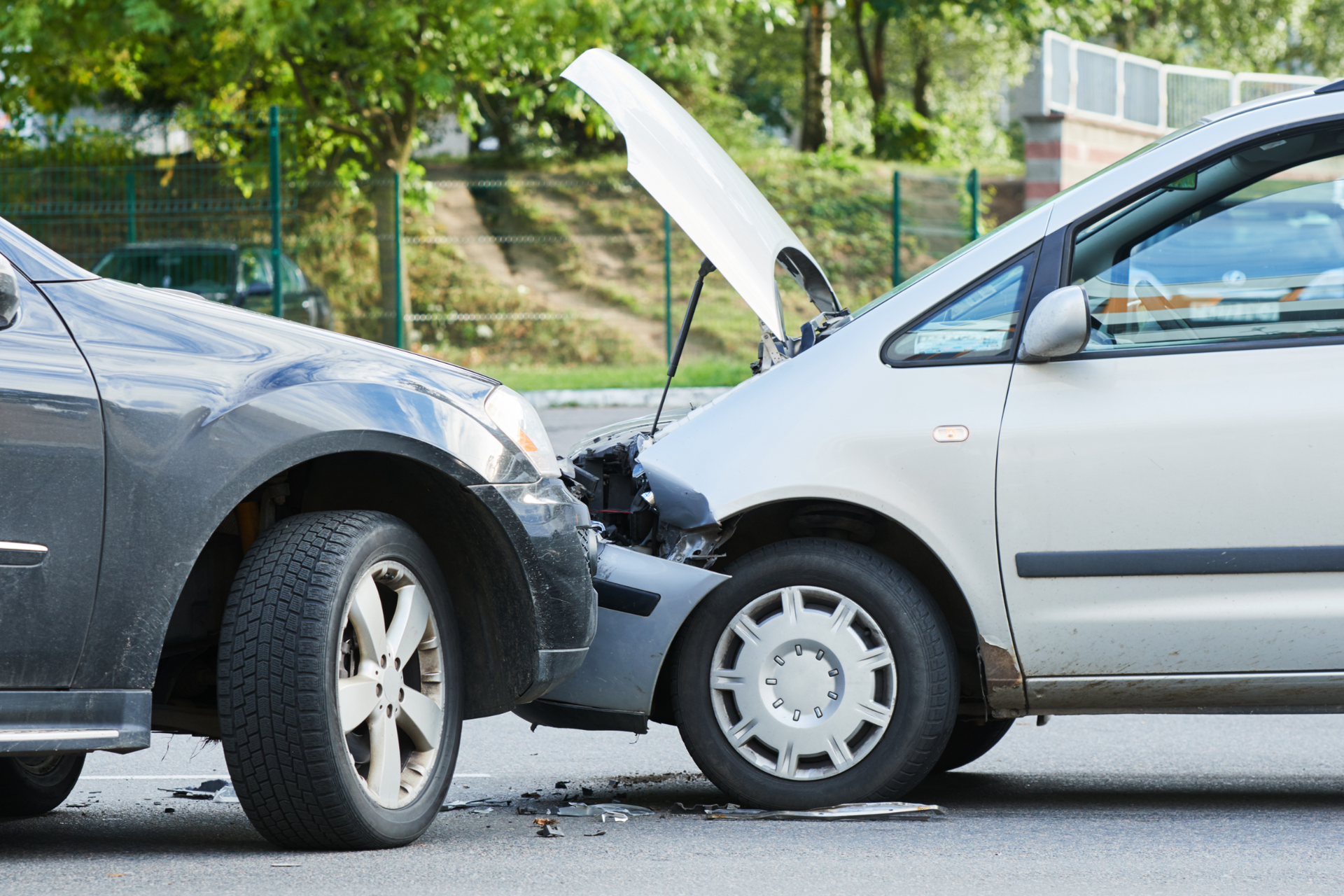 A dark car and a light-colored car with its hood popped open are involved in a head-on collision on a road.