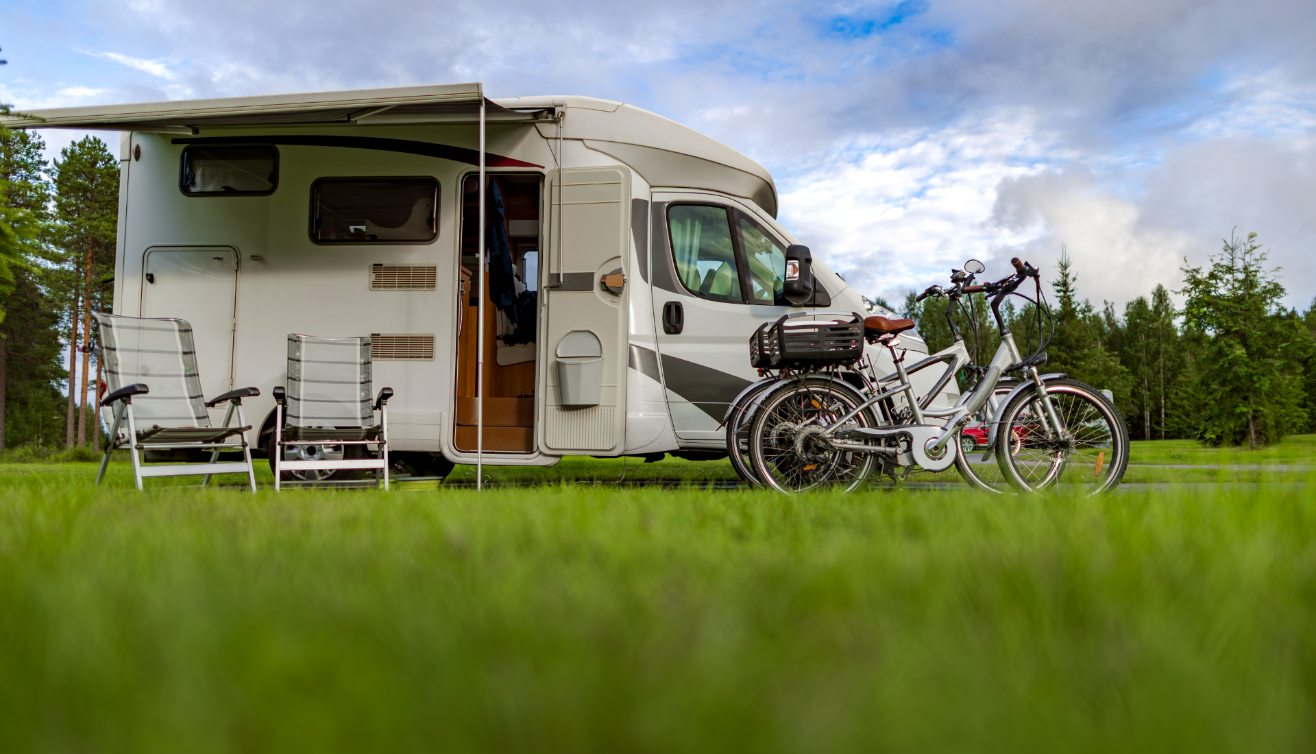 A white camper van parked on a green field with two folded camping chairs and two bicycles mounted on a rear rack.