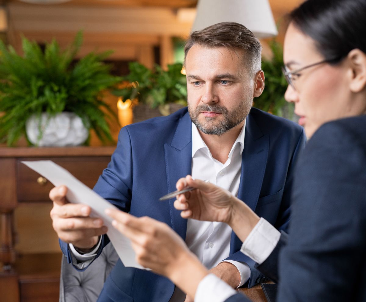 Two professionals in business attire review a document together in a workspace with indoor plants.
