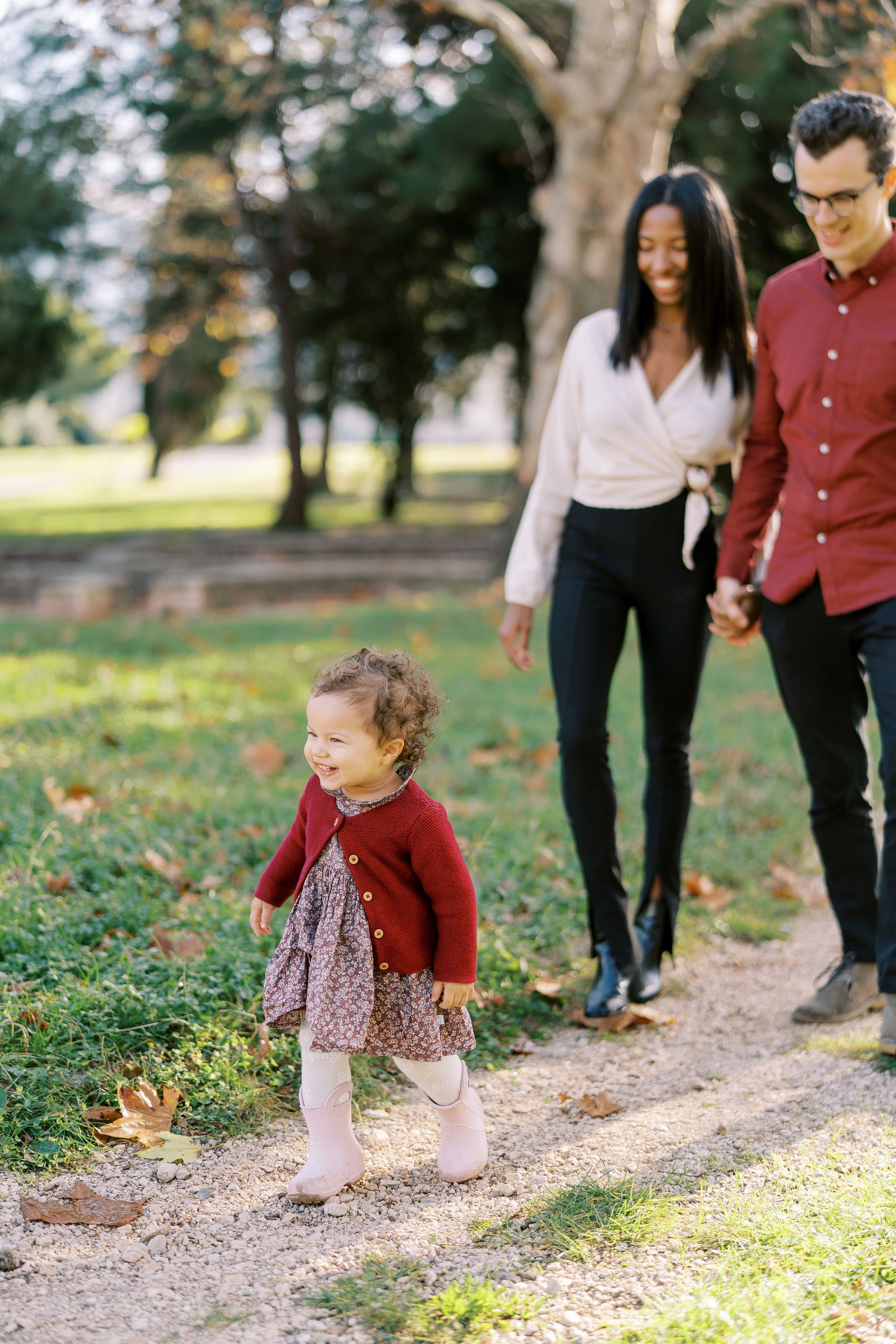 Family walks along a path in a park; child in front smiles, parents holding hands follow.