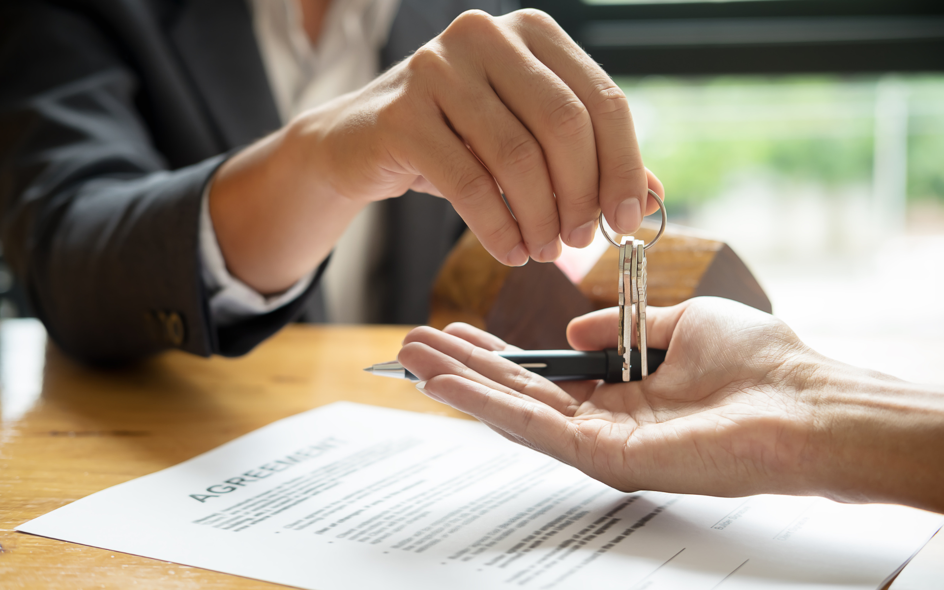 Person handing keys to another person over a table with a document, symbolizing a real estate transaction.