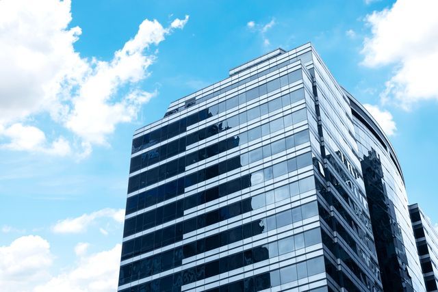Modern glass skyscraper against a blue sky with fluffy clouds.
