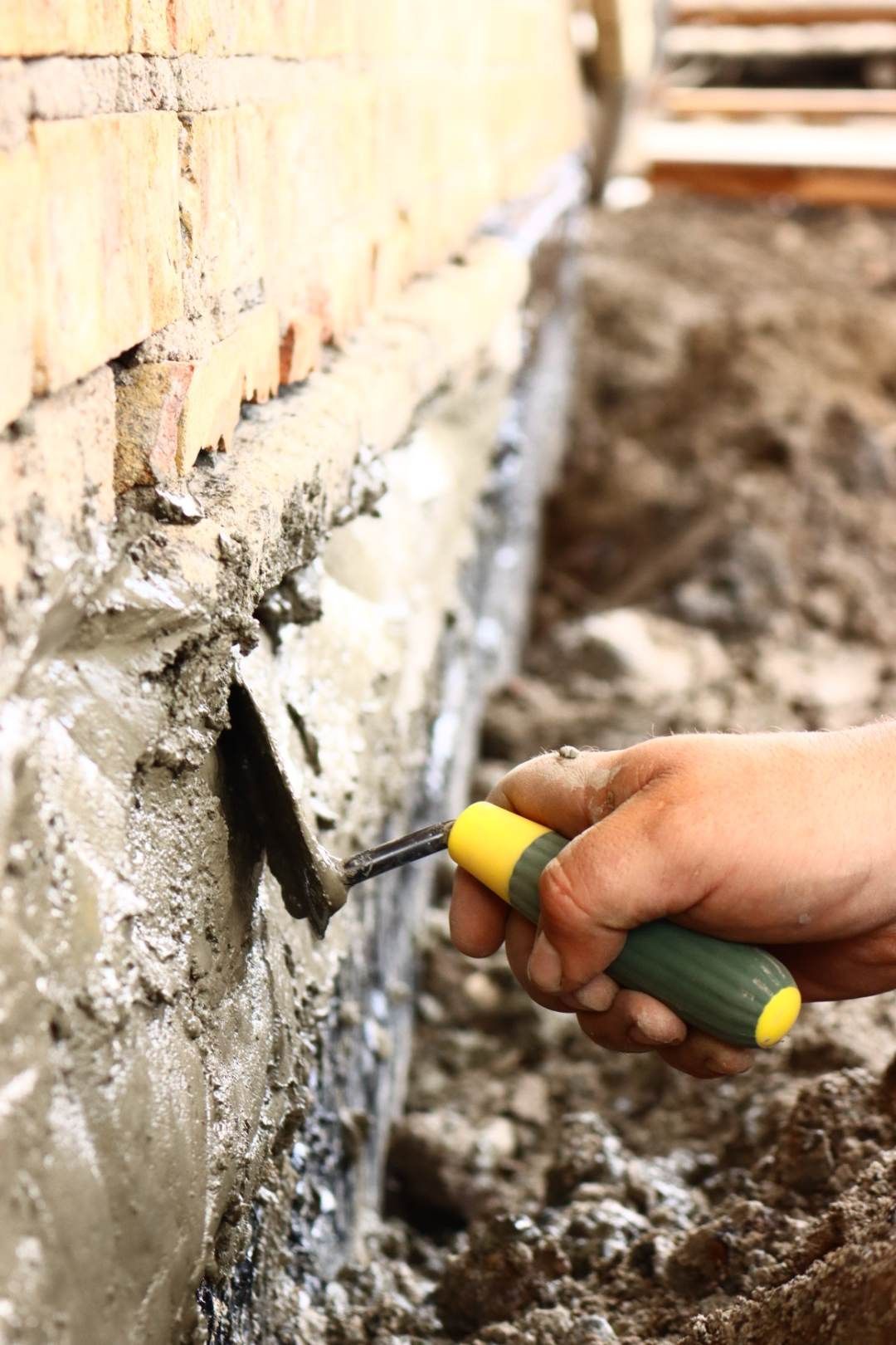 Une personne utilise une truelle pour étaler du béton sur un mur de briques.