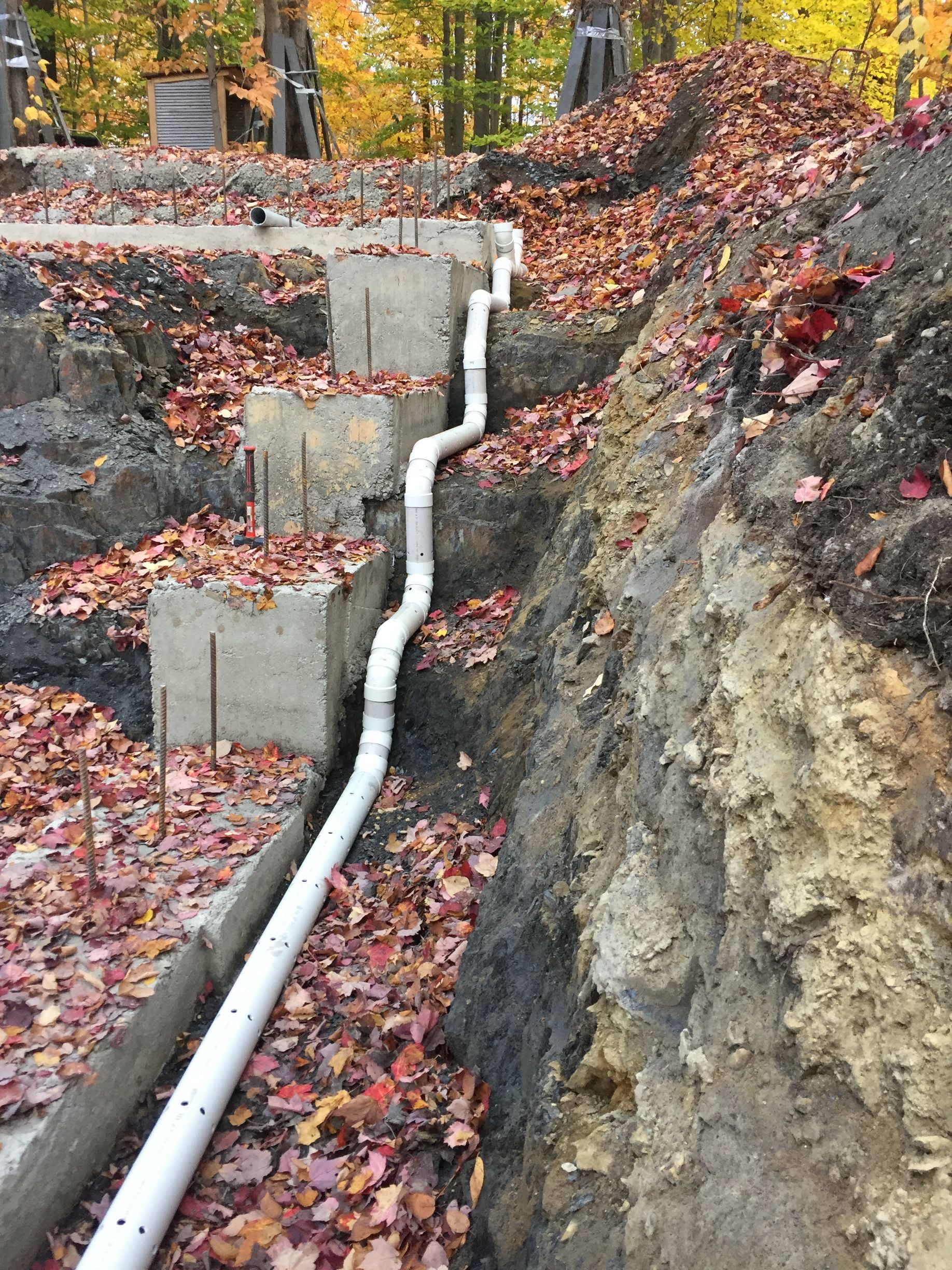 Un tuyau blanc repose dans la terre à côté d'un tas de feuilles.