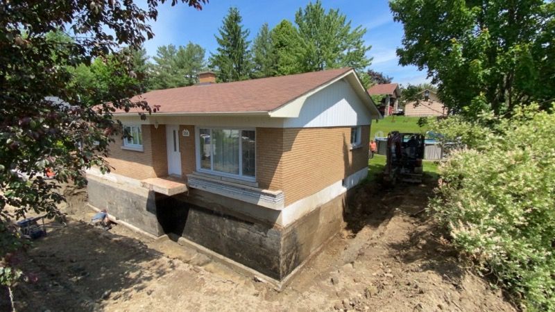 Une maison en brique avec un toit rouge se trouve au sommet d'une colline de terre.