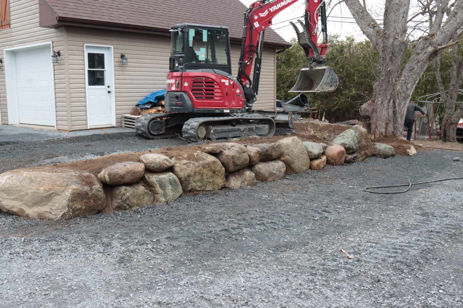 Une excavatrice rouge travaille sur une paroi rocheuse devant une maison.