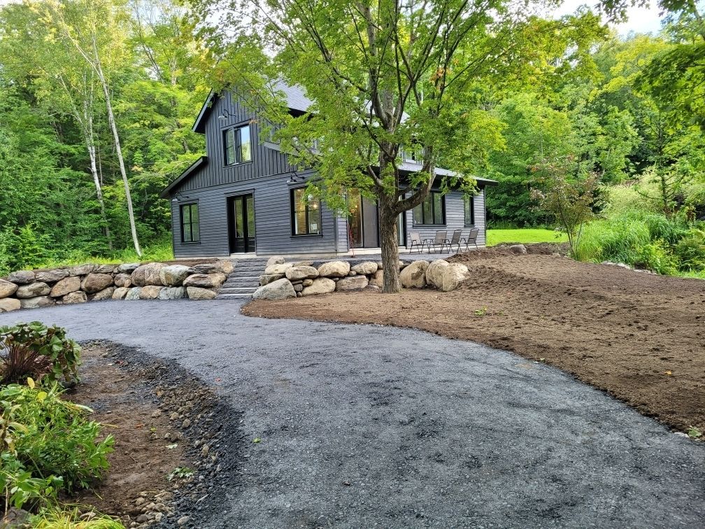 Une maison noire est située au sommet d'une colline de terre au milieu d'une forêt.
