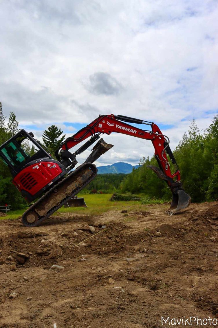 Une excavatrice rouge est assise au sommet d'un champ de terre.