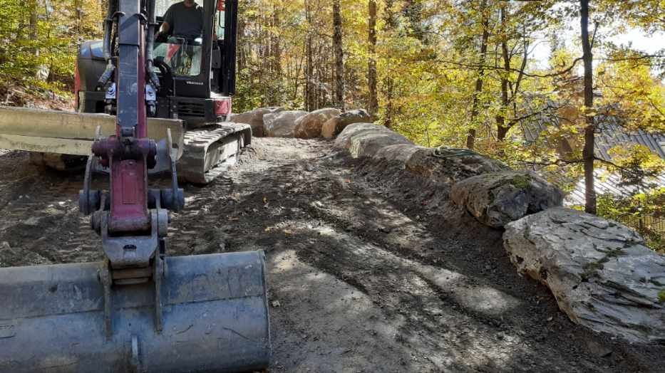 Un homme conduit un bulldozer sur un chemin de terre dans les bois.