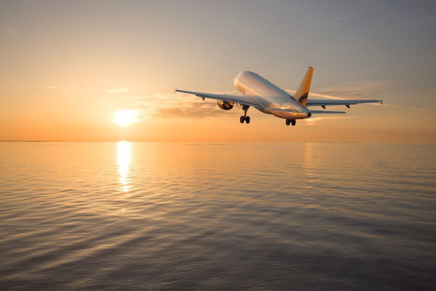 An airplane is flying over the ocean at sunset.