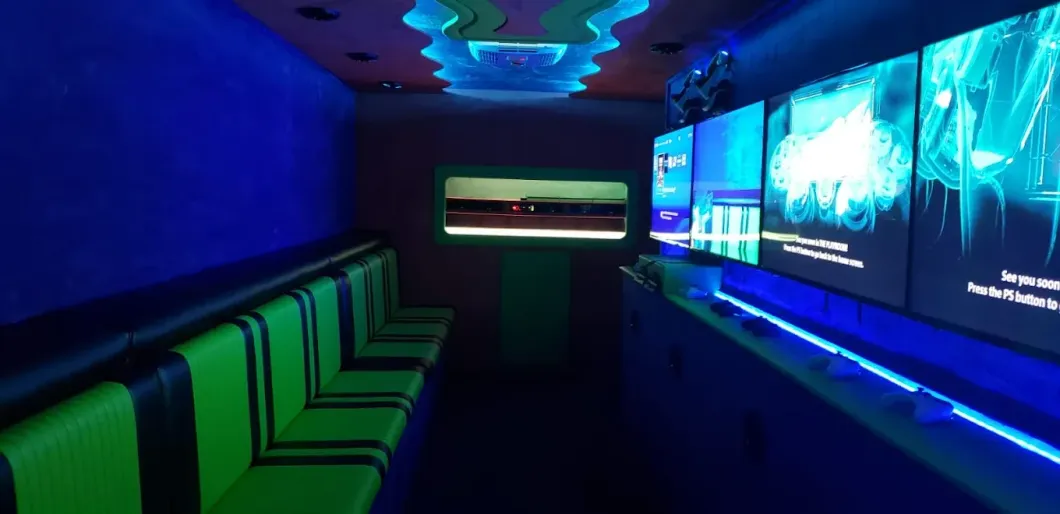 Interior of a game truck with green seating, blue walls, and screens displaying images.