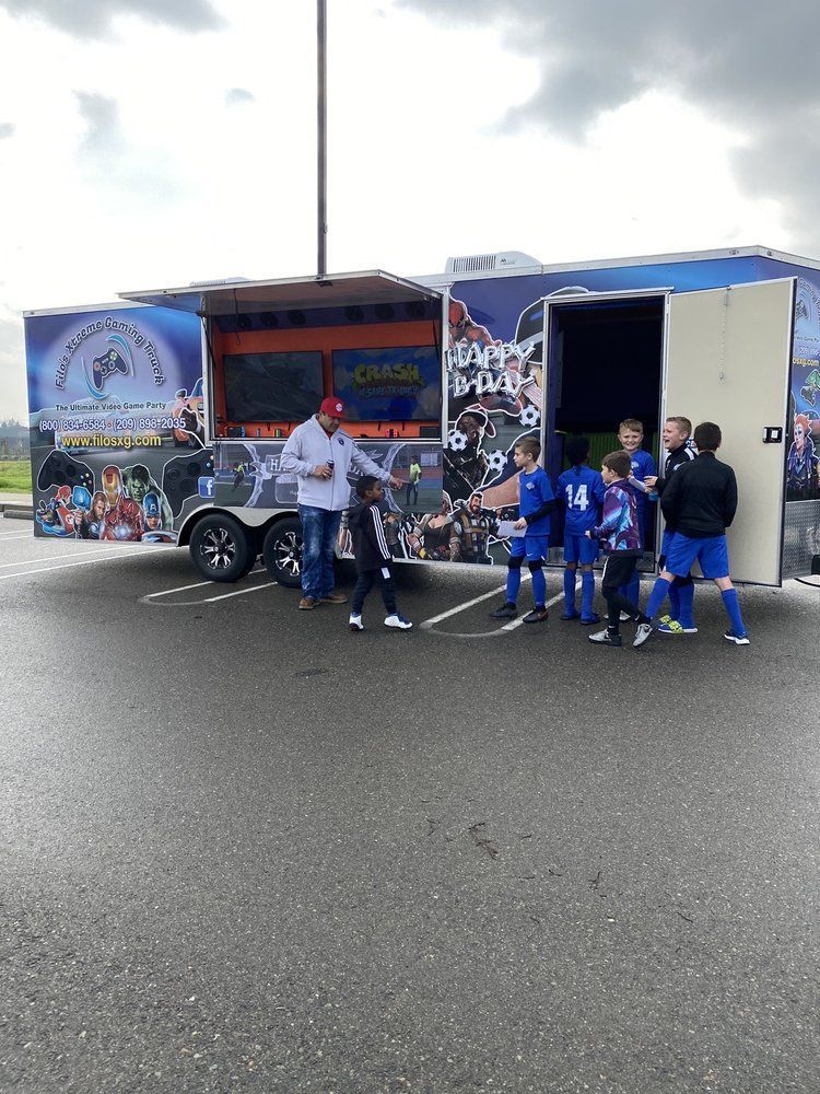 Soccer players in blue uniforms by a trailer with a coach in a parking lot.