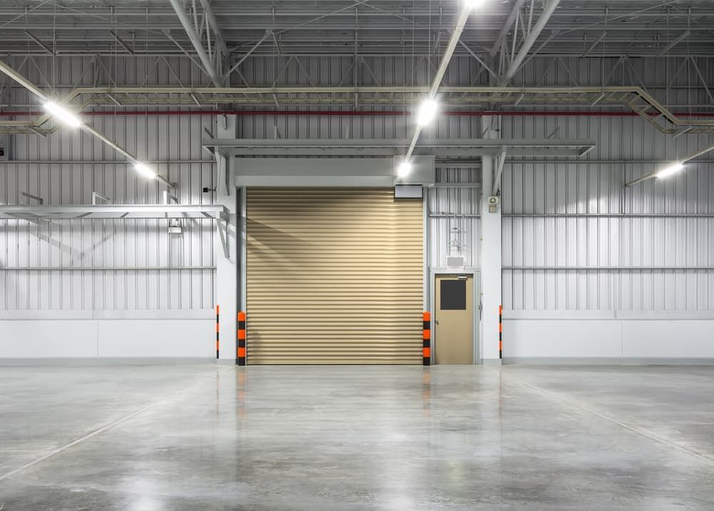 An Empty Warehouse With A Roller Door And A Concrete Floor — The Roller Door Man NQ In Portsmith, QLD