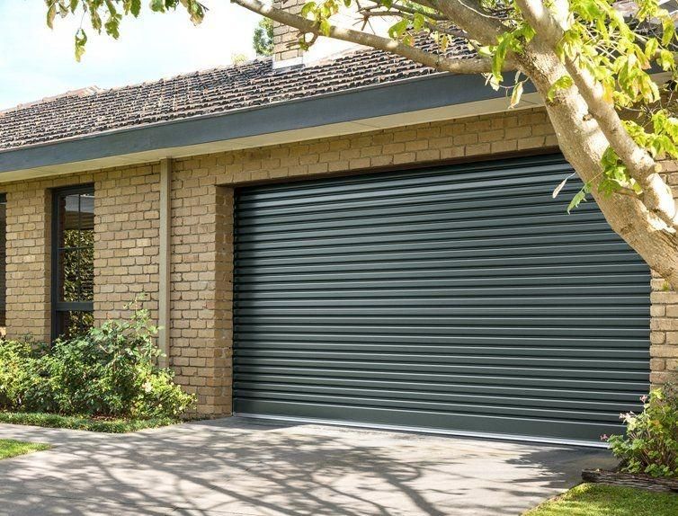 A Brick House With A Black Garage Door And A Tree In Front Of It — The Roller Door Man NQ In Portsmith, QLD