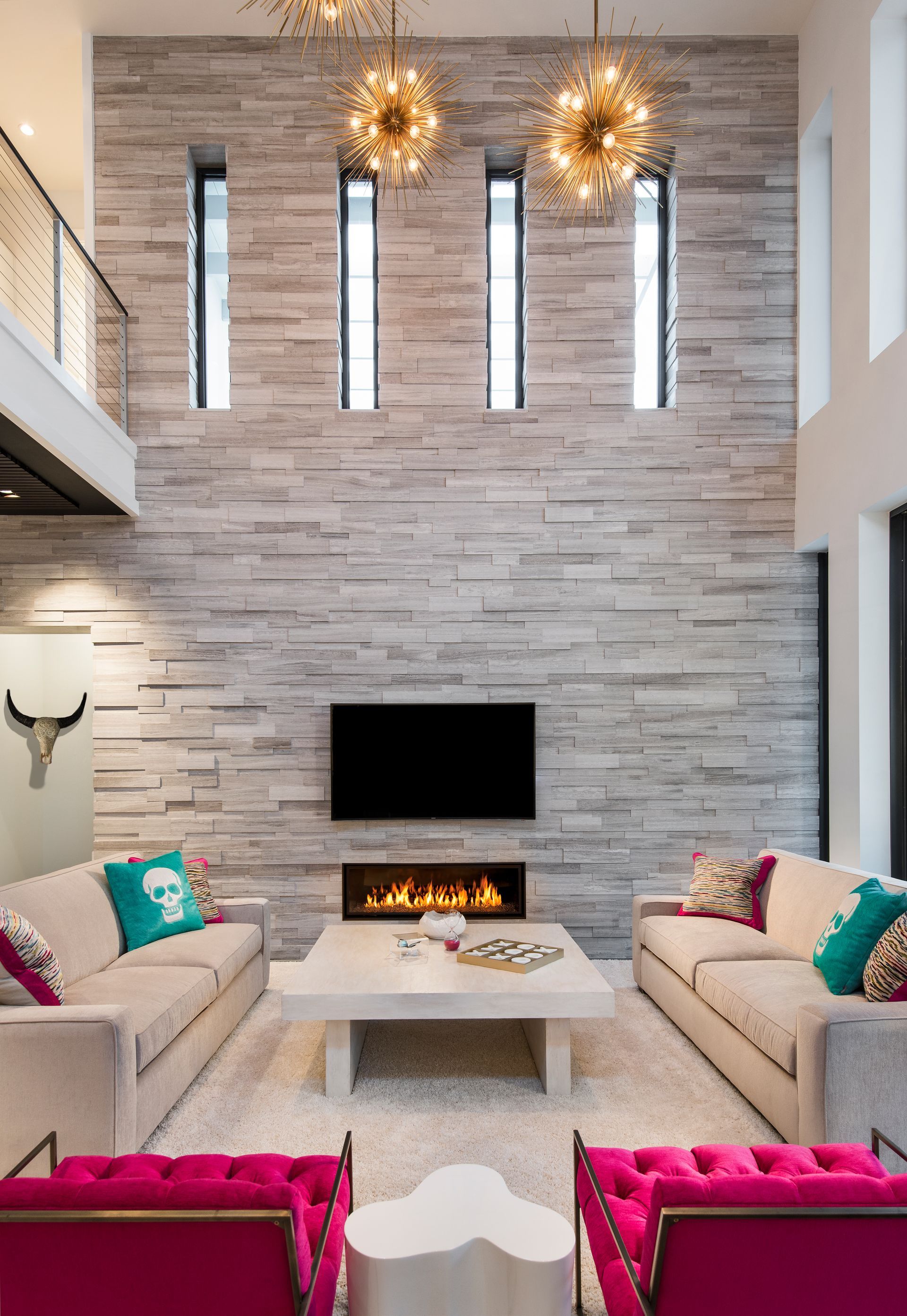 Modern living room with stone accent wall, fireplace, TV, neutral sofas, and vibrant pink and turquoise accents.