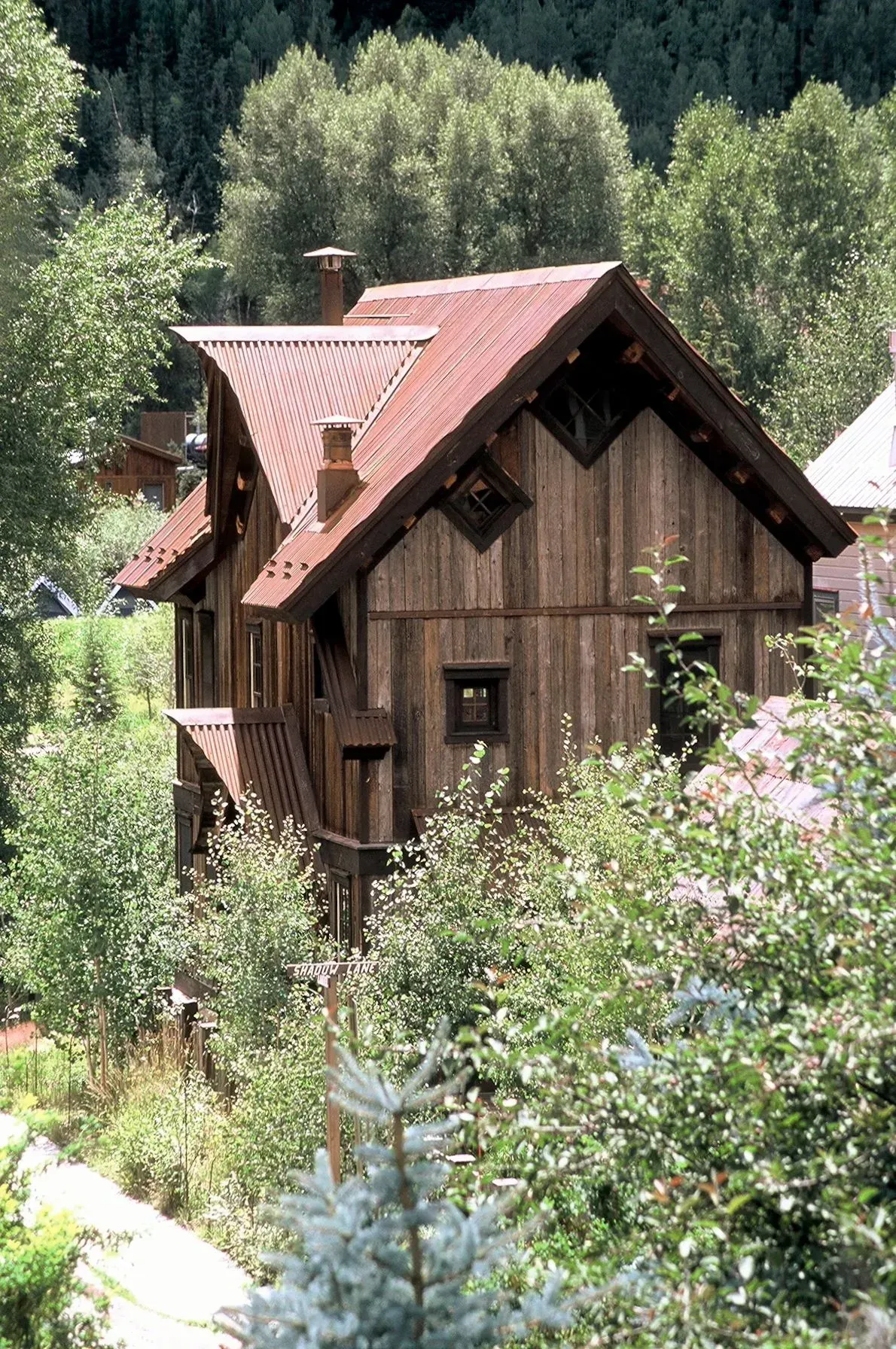 Rustic wooden house with a red metal roof, surrounded by trees and foliage.