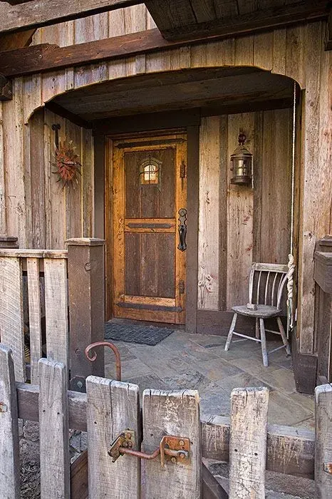 Rustic wooden porch with door, chair, and weathered fence.