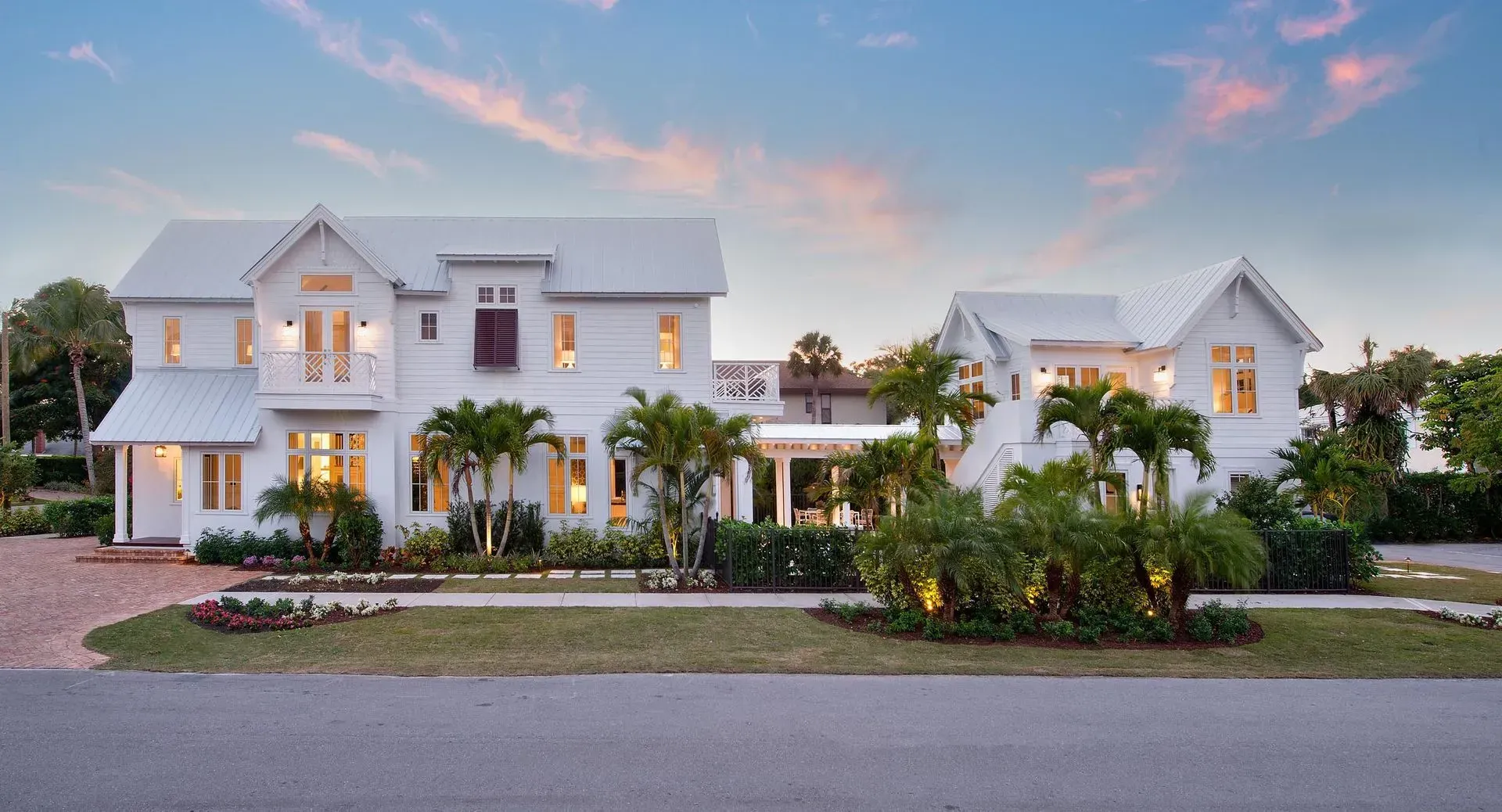 White two-story house with a matching smaller building, palm trees, and landscaped yard.