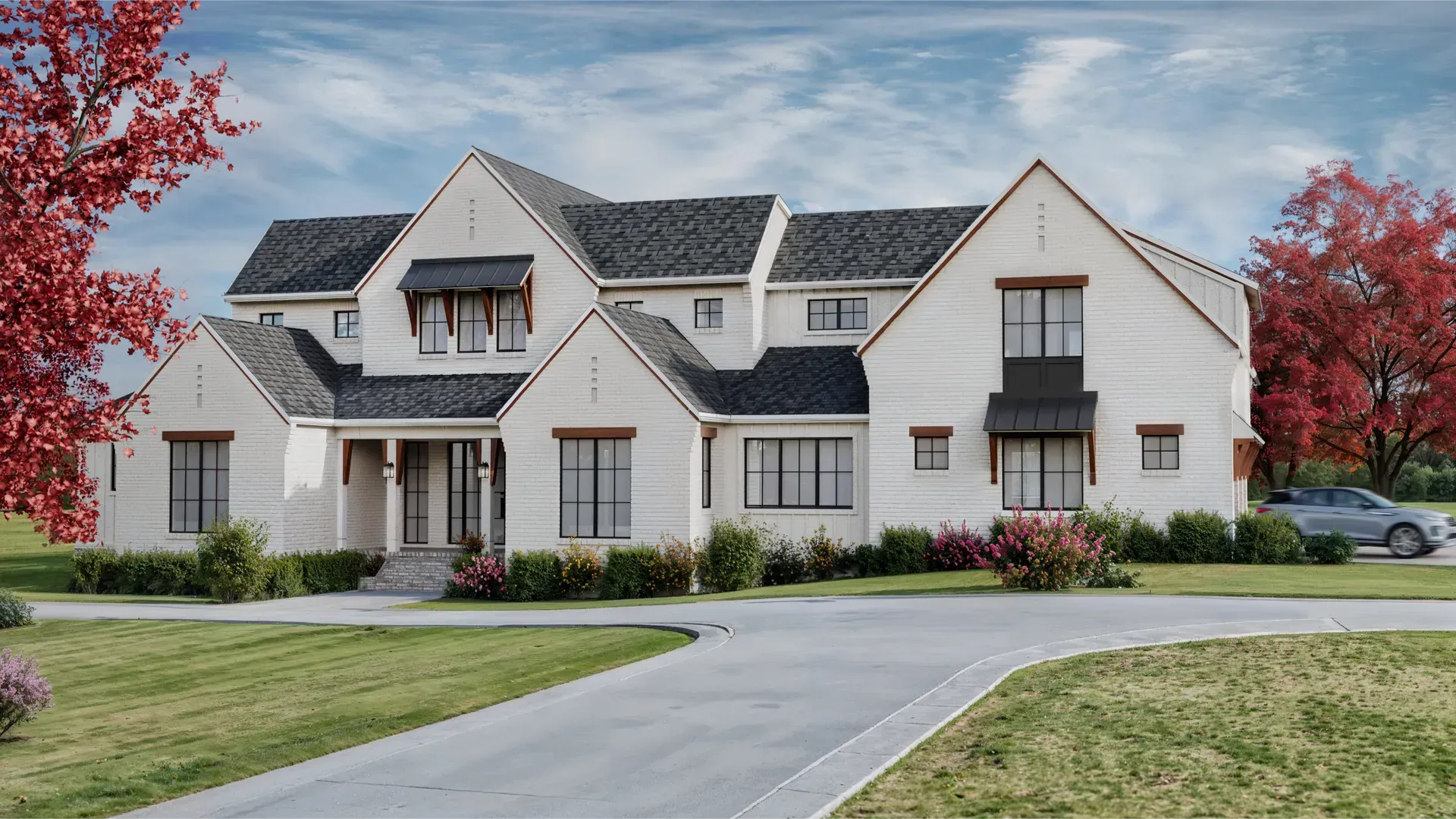 White two-story house with a black roof, driveway, and red-leafed trees. A car is parked nearby.