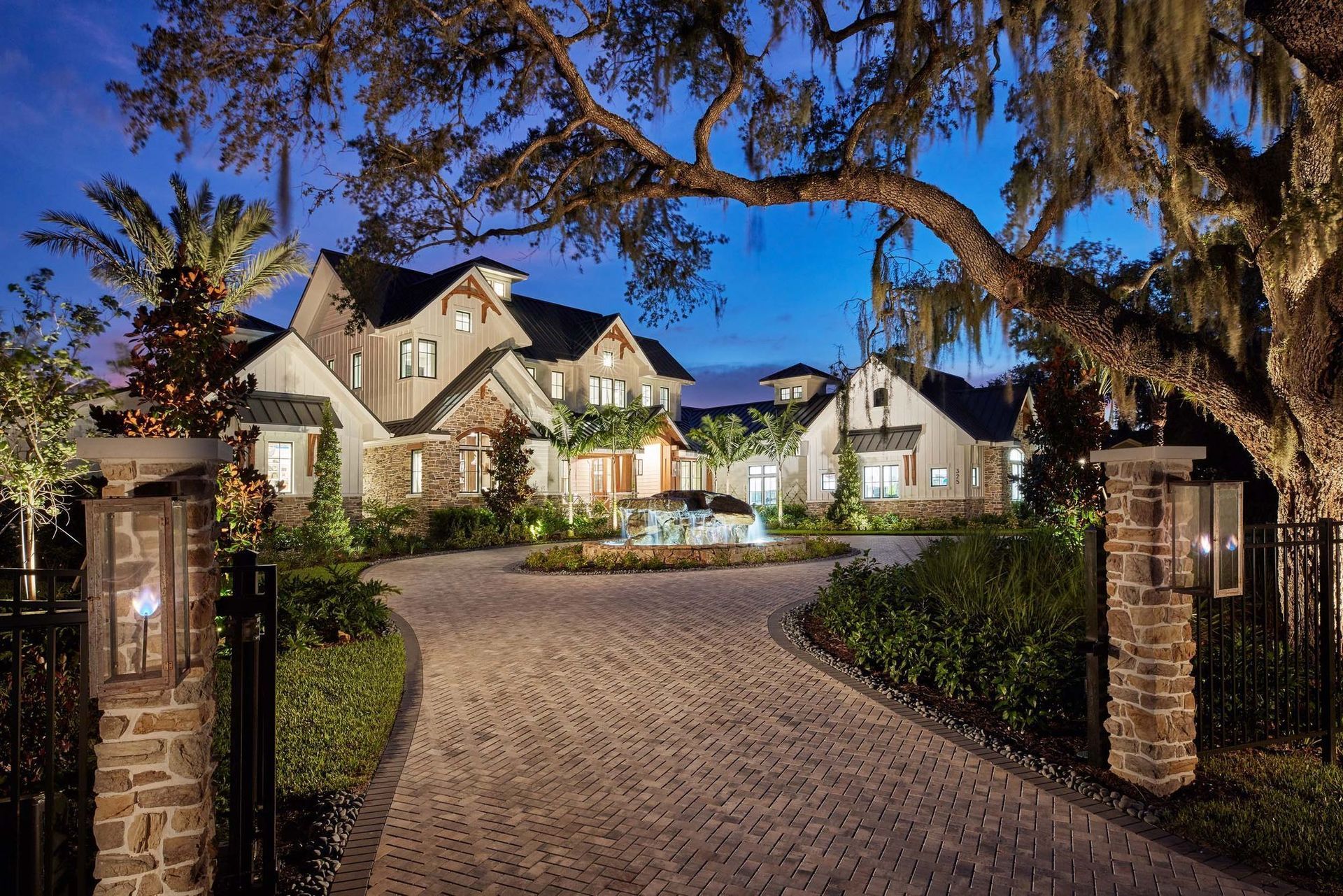 Elegant home with stone accents and a curved brick driveway, lit at dusk.
