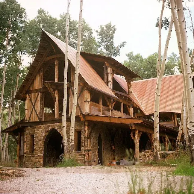 Rustic wooden house with stone base and copper roof, nestled among trees.