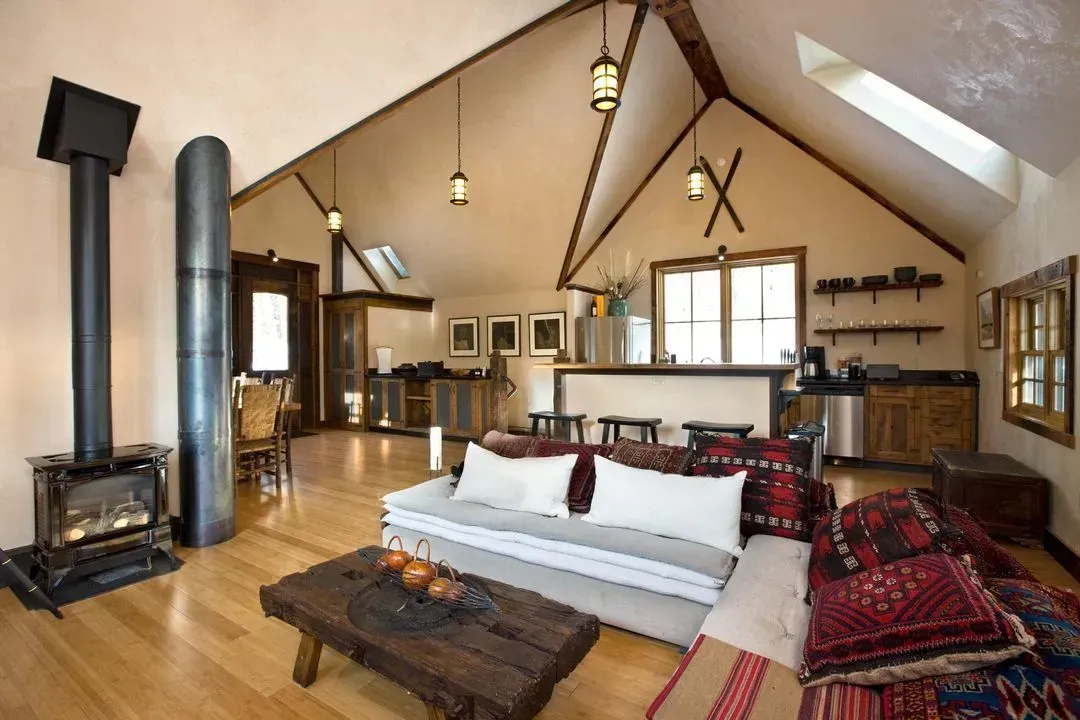 Cozy living room with vaulted ceiling, wood stove, hardwood floors, and rustic furniture.