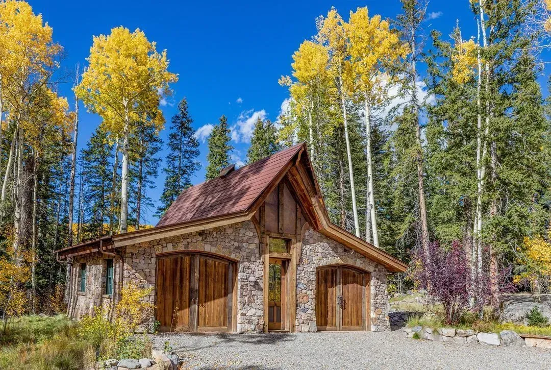 Stone garage with wooden doors and red tile roof, surrounded by golden aspen trees under a blue sky.