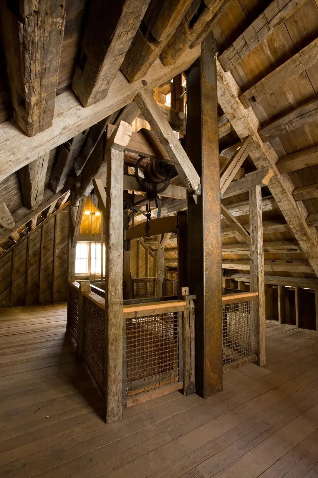 Wooden attic with a cage-like elevator, dark beams, and a window.