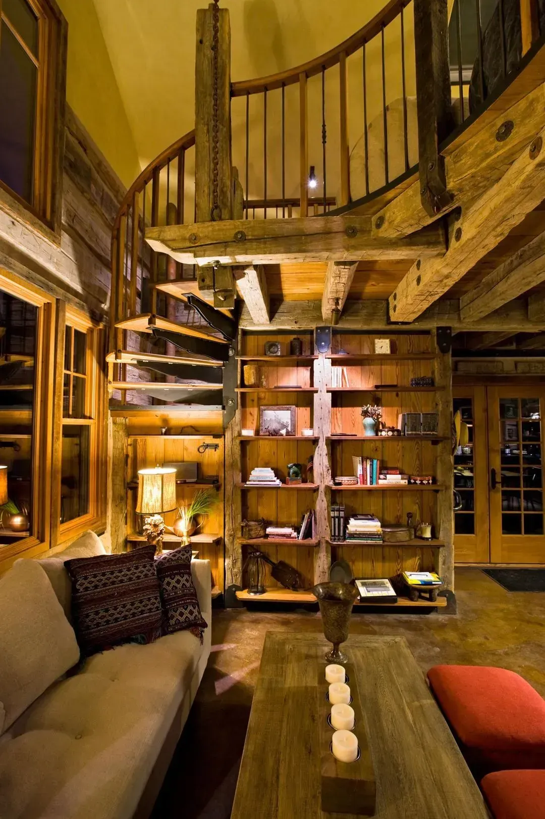 Rustic interior with spiral staircase, bookshelf, sofa, and wood beams.