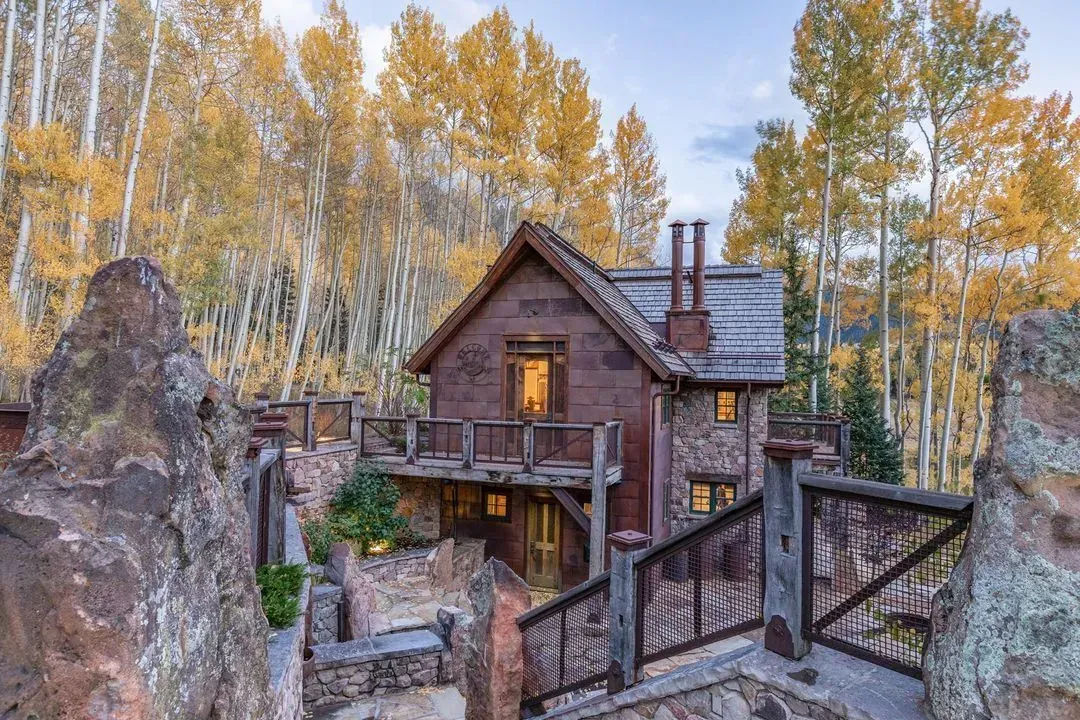 Stone house nestled in rocky terrain with wooden accents, surrounded by yellow aspens.
