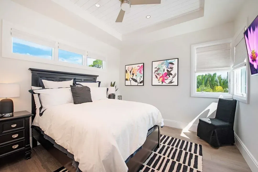 Bedroom with a black bed frame, nightstand, and colorful artwork. Features windows and a striped rug.