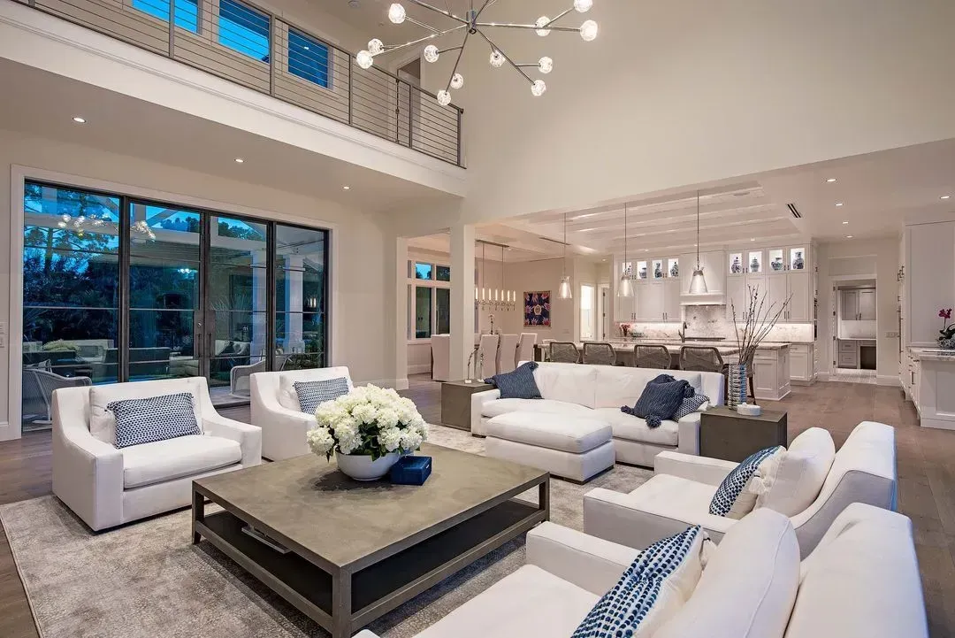 Spacious white living room with high ceilings, glass doors, and modern furniture.