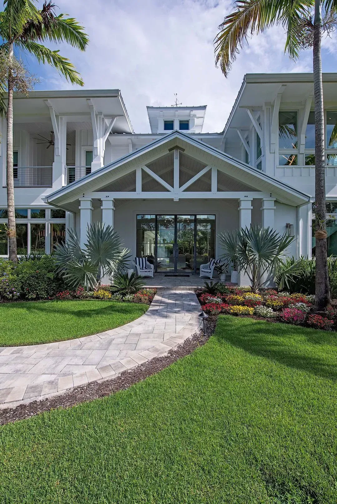 Stone path leads to a white coastal home with palm trees and a colorful garden.