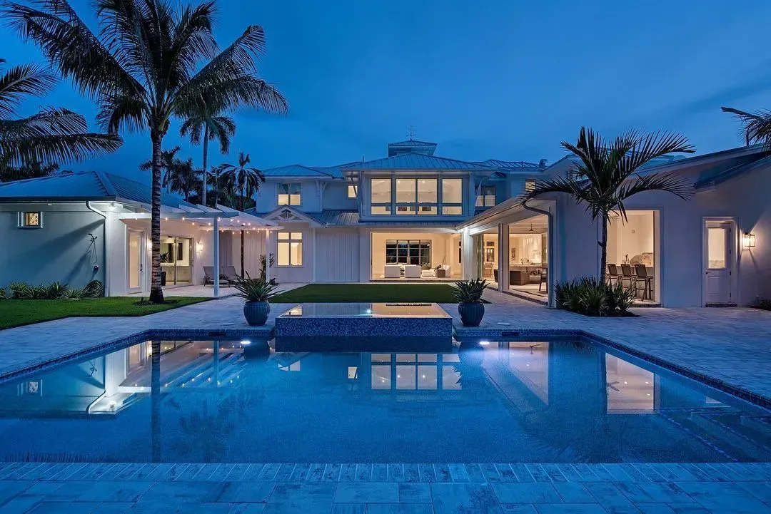 Luxury home at dusk with a pool and palm trees, illuminated by blue lights.