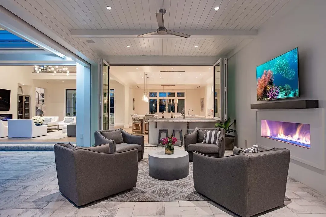 Outdoor patio with seating, fireplace, and TV, connecting to a home's interior.