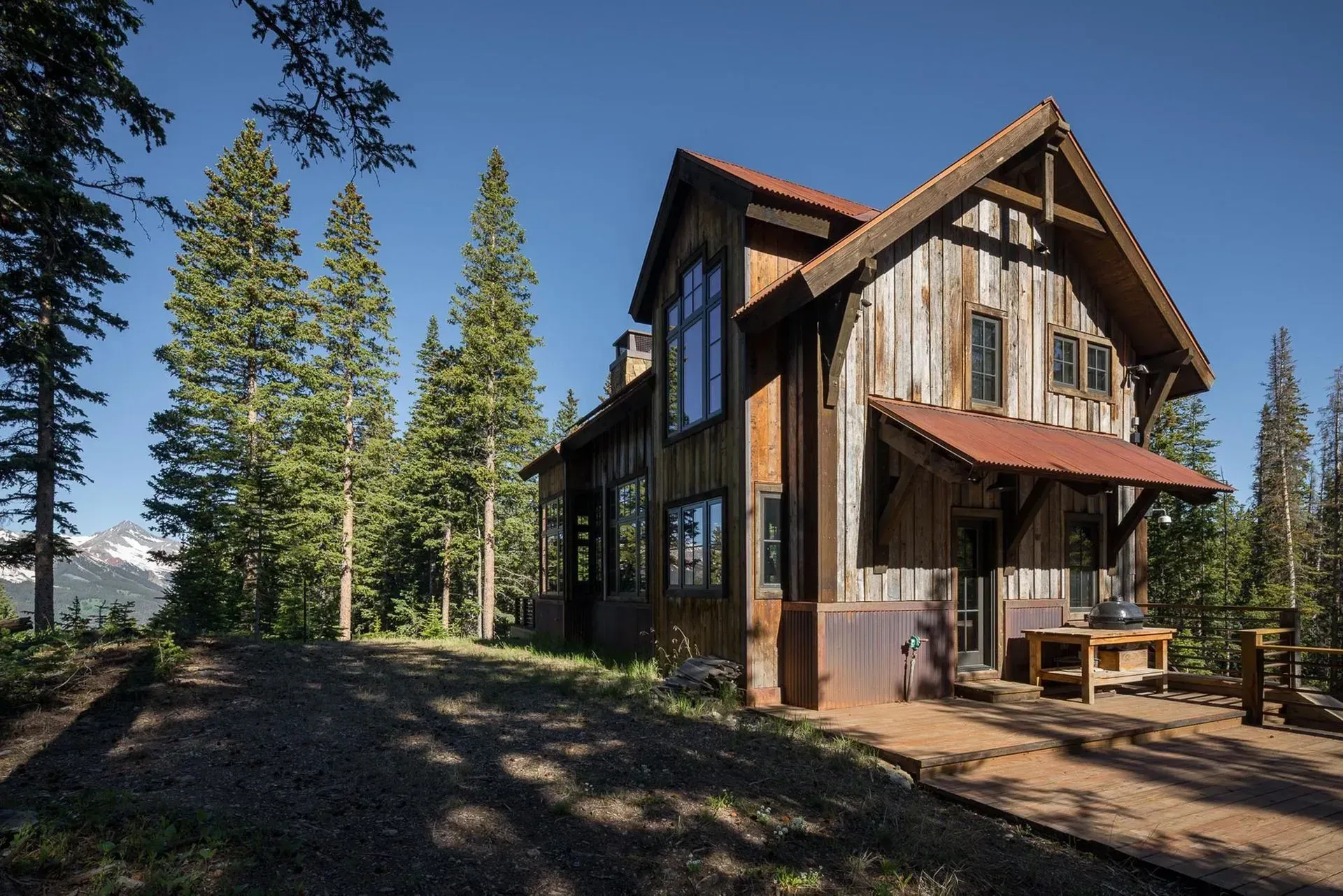 Rustic cabin with weathered wood siding and red metal roof surrounded by trees under a blue sky.