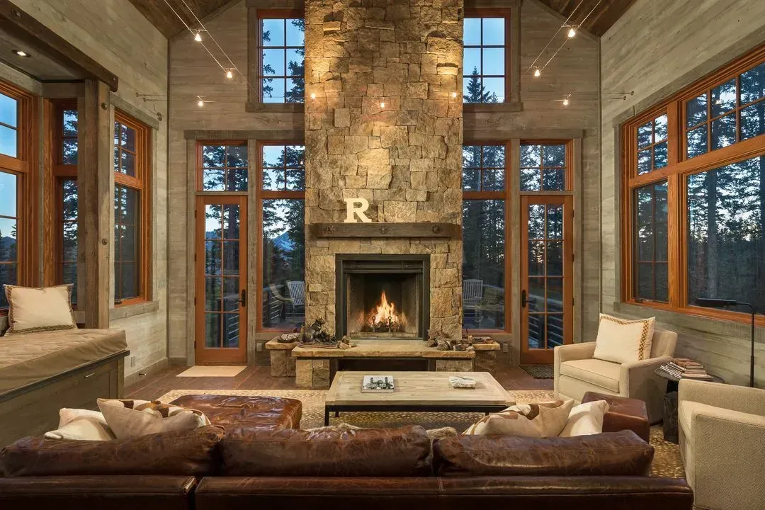 Cozy living room with stone fireplace, large windows, leather sofa, and armchairs.