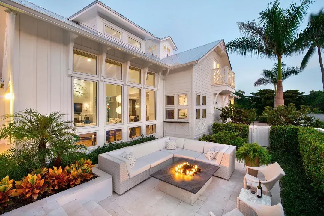 White house exterior with outdoor seating around a fire pit, surrounded by lush green landscaping.