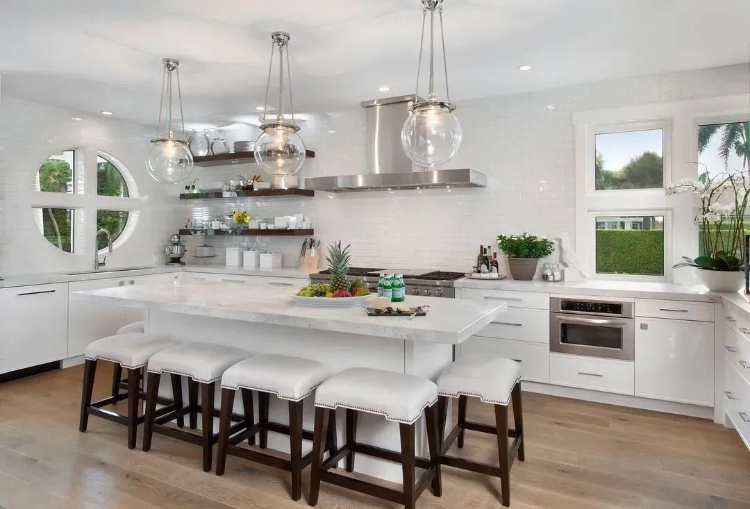 Bright white kitchen with island seating, stainless steel appliances, and wooden floors.