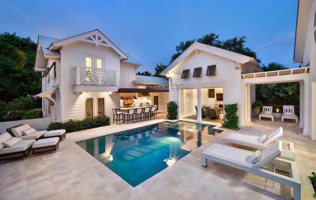 Luxury villa with a pool, lounge chairs, and an outdoor bar, lit by evening lights.