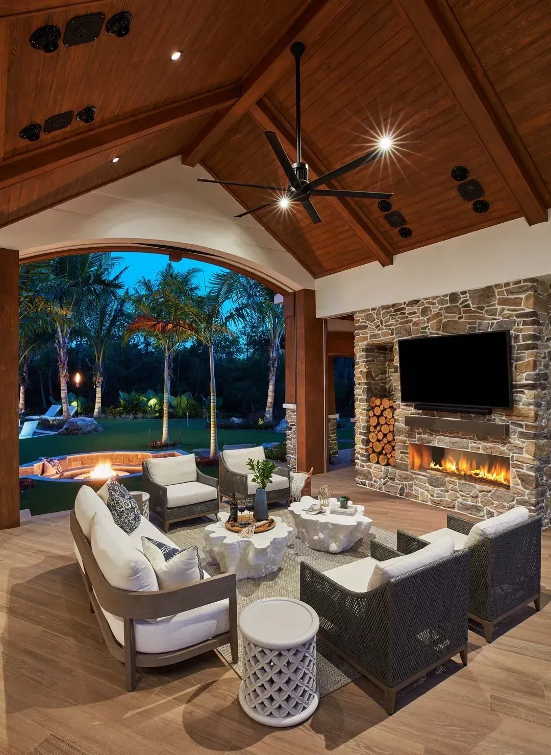 Outdoor living space with seating, fireplace, and TV under a wood ceiling.