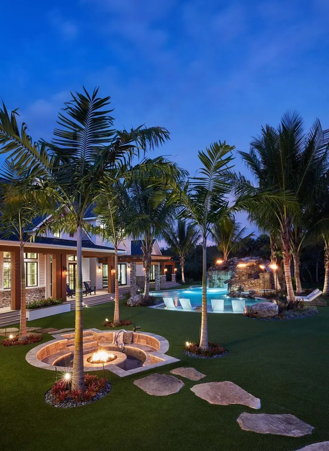 Backyard at dusk with fire pit, pool, and palm trees.
