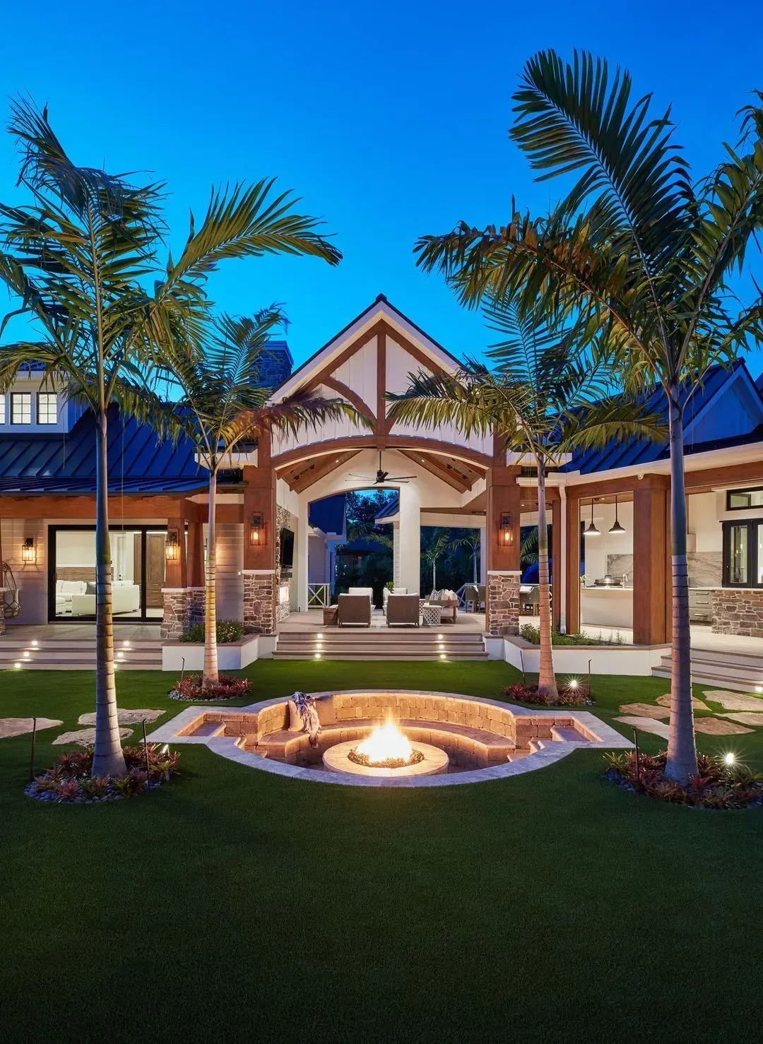 Luxury backyard at dusk: fire pit, palm trees, open-air living space, blue sky.