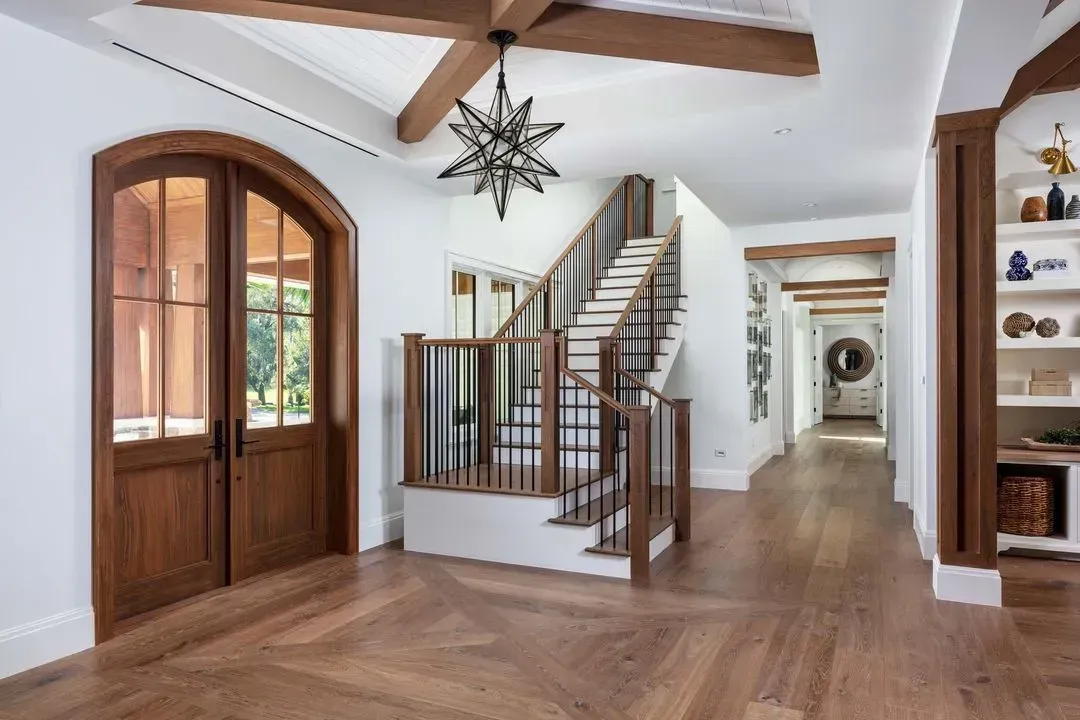 Wooden foyer with double doors, staircase, and beamed ceiling; wood floors and white walls.