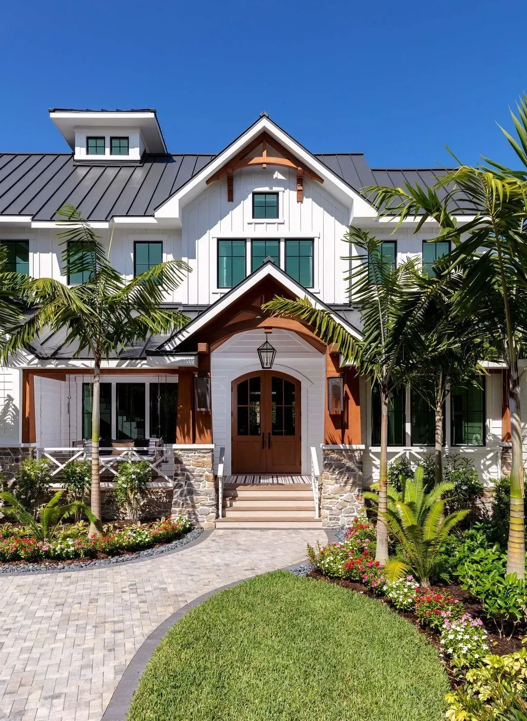 White farmhouse with brown trim, palm trees, and brick pathway under a bright blue sky.