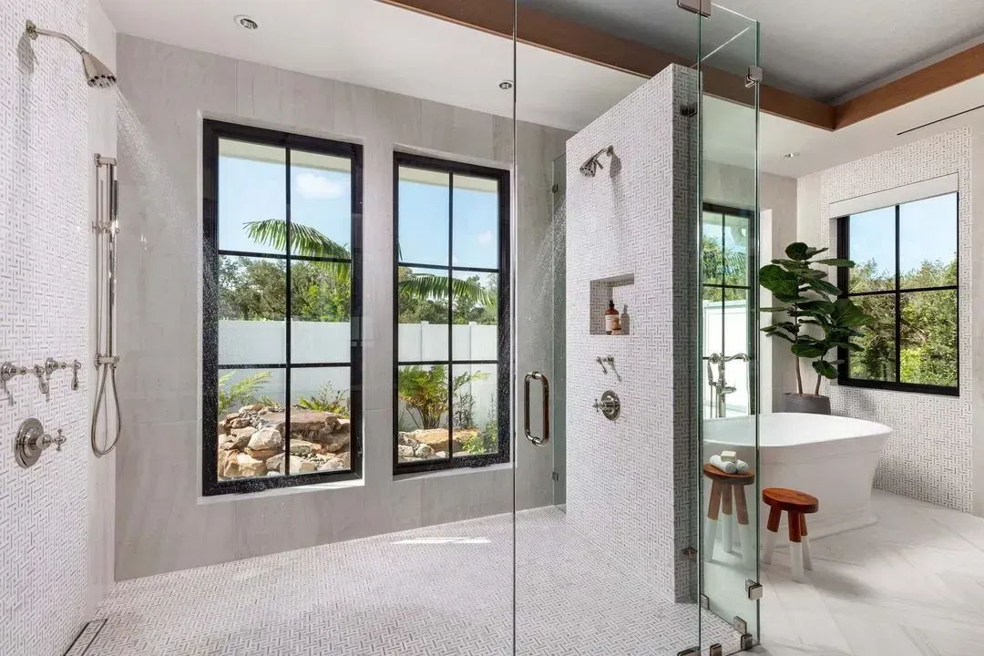 Luxurious bathroom with windows, freestanding tub, glass shower, and mosaic tile.