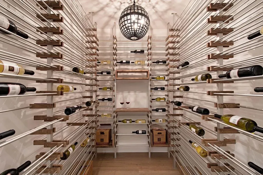 Wine cellar with rows of bottles on metal racks and wooden shelves. A decorative hanging light fixture is visible.