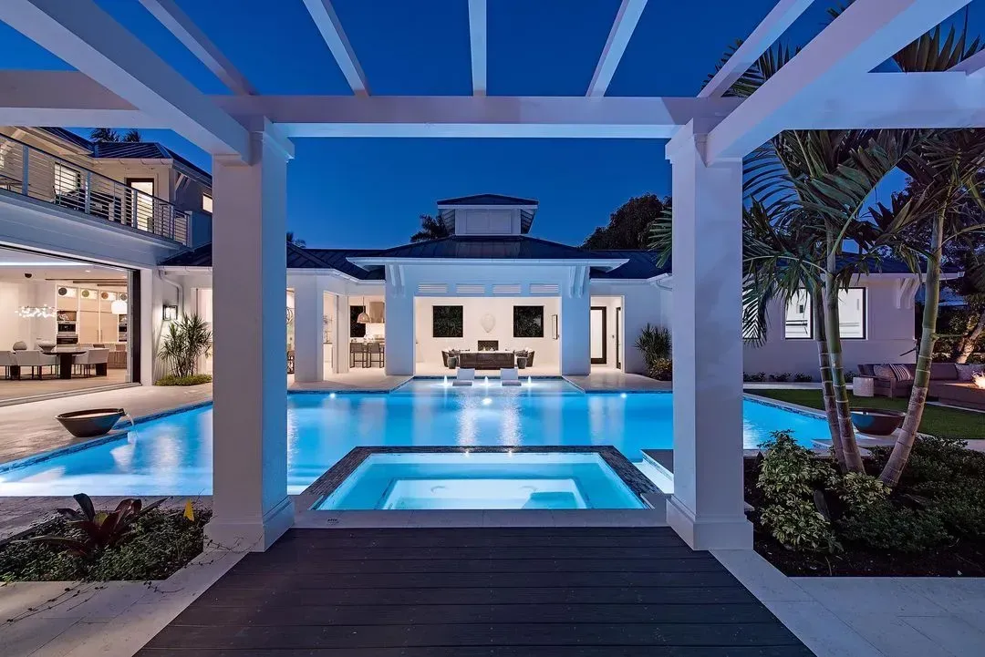 Nighttime view of a luxury pool and spa area with a white, modern house in the background.