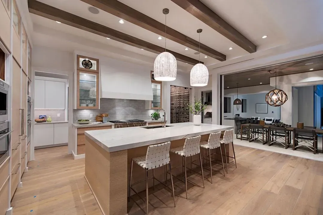 Modern kitchen with island, pendant lights, wooden beams, and open dining area.