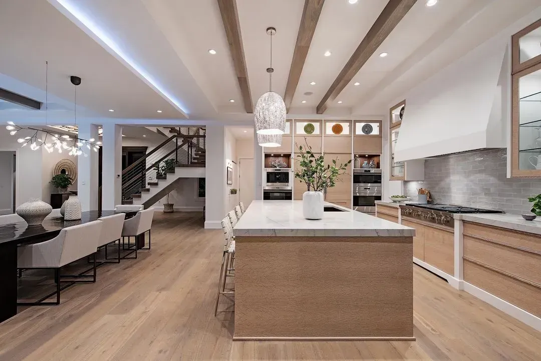 Spacious kitchen with wood cabinets, island, and dining area. Light wood floors and exposed beams.